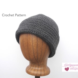 May include: Crochet pattern for a gray beanie hat. The hat is on a wooden mannequin head. The text "Girlpower Designs" is in the lower right corner of the image.
