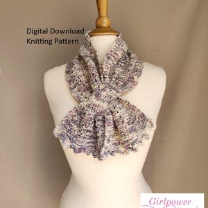 May include: A hand-knitted scarf in shades of purple, cream, and lavender, displayed on a mannequin. The scarf features a textured stitch pattern and a ruffled edge. Text on the image reads "Digital Download Knitting Pattern" and "Girlpower Designs".