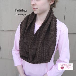 Może przedstawiać: Ciemnobrązowy dzianinowy szalik typu infinity. Szalik jest owinięty wokół szyi i ramion. Słowa "Knitting Pattern" znajdują się w lewym górnym rogu. Logo Girlpower Designs znajduje się w prawym dolnym rogu.