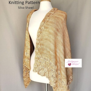 Pode incluir: Um xale de malha em tons de ouro e bege, exibido em um manequim. O xale apresenta um padrão decorativo de folhas nas bordas e está rotulado como "Knitting Pattern Silva Shawl". O logotipo Girlpower Designs é visível.