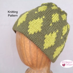 May include: Knitting pattern for a green and yellow beanie hat with a leaf design. The hat is on a wooden mannequin head. "Girlpower Designs" is written in the bottom right corner of the image.