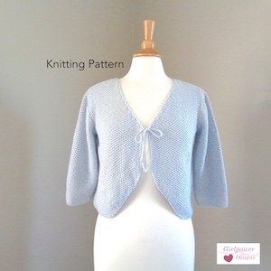May include: Knitting pattern for a light blue cropped cardigan with a tie at the neckline. The pattern is called "Girlpower Designs".