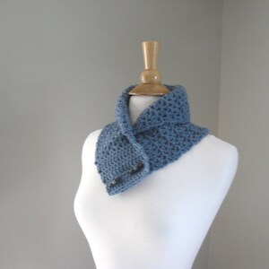 May include: A blue crochet cowl scarf with a button closure, displayed on a white mannequin. The scarf is a solid blue color and appears to be handmade. The cowl is designed to be worn around the neck.