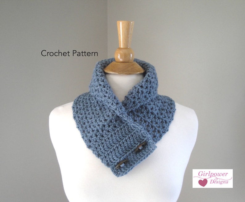 May include: A blue crocheted cowl with two wooden buttons, displayed on a white mannequin. The text "Crochet Pattern" is above the cowl. The "Girlpower Designs" logo is in the bottom right corner.