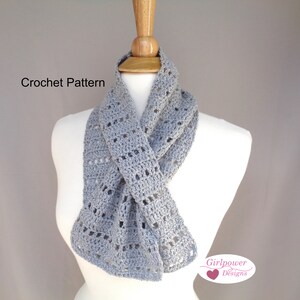 Puede incluir: Una bufanda de ganchillo gris con un patrón de encaje. La bufanda se muestra en un maniquí blanco. El texto "Crochet Pattern" es visible en la parte superior de la imagen. El texto "Girlpower Designs" es visible en la parte inferior de la imagen.