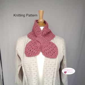 Puede incluir: Bufanda de punto color rosa polvoriento con un diseño único en forma de pétalo. La bufanda se muestra en un maniquí, mostrando su patrón de punto texturizado y detalles calados. El texto "Knitting Pattern" es visible.