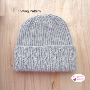 May include: A gray knitted beanie with a cable knit pattern on the brim. The beanie is on a wooden surface. The text "Knitting Pattern" is visible at the top of the image.