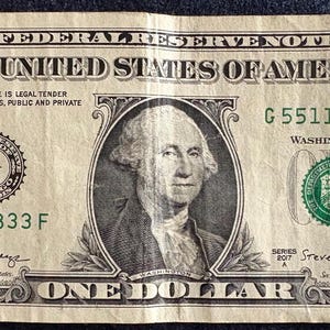 May include: A one-dollar bill featuring a portrait of George Washington. The bill has the text "THE UNITED STATES OF AMERICA" and "ONE DOLLAR". The bill is green and black with the serial number G55113833F.