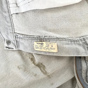 Pode incluir: Um par de cal&ccedil;as de ganga Wrangler cinzentas claras com uma mancha castanha. As cal&ccedil;as de ganga t&ecirc;m um fecho de correr e um r&oacute;tulo que diz "Wrangler Men's Regular Fit Style 309GRY Waist 34 Length 36 Machine Wash Inside Out With Like Colors Tumble Dry Remove Promptly Made In U.S.A. L.N. 2"