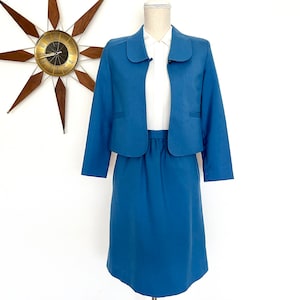 May include: A blue skirt suit with a peter pan collar jacket. The jacket has a white button-up shirt underneath.