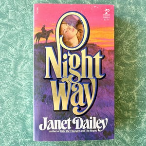 May include: A paperback book cover with a purple background and gold lettering. The title is "Night Way" by Janet Dailey. The author is also noted as the author of "Ride the Thunder and The Rogue".