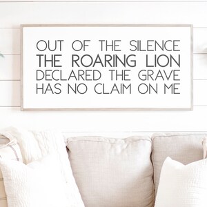 Może przedstawiać: Wydruk w ramie z tekstem "OUT OF THE SILENCE THE ROARING LION DECLARED THE GRAVE HAS NO CLAIM ON ME" wiszący na białej ścianie z desek drewnianych nad beżową kanapą z białymi i brązowymi wzorzystymi poduszkami.