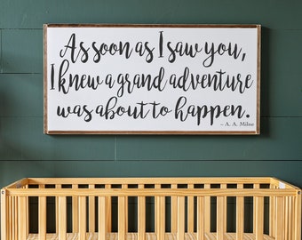 Puede incluir: Una cuna de madera con una sábana estampada en amarillo y marrón. La cuna está frente a una pared verde con un cartel blanco que dice "As soon as I saw you, I knew a grand adventure was about to happen. - A.A. Milne".