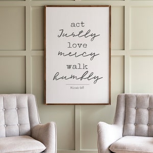 May include: A framed print with a white background and black text that reads "act justly love mercy walk humbly Micah 6:8". The print is hanging on a sage green wall with two light gray chairs in front of it.