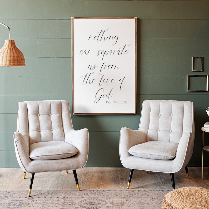 May include: A white framed sign with the text "nothing can separate us from the love of God" and the scripture reference "Romans 8:36". Two light gray upholstered armchairs with tufted backs and black legs sit in front of the sign.