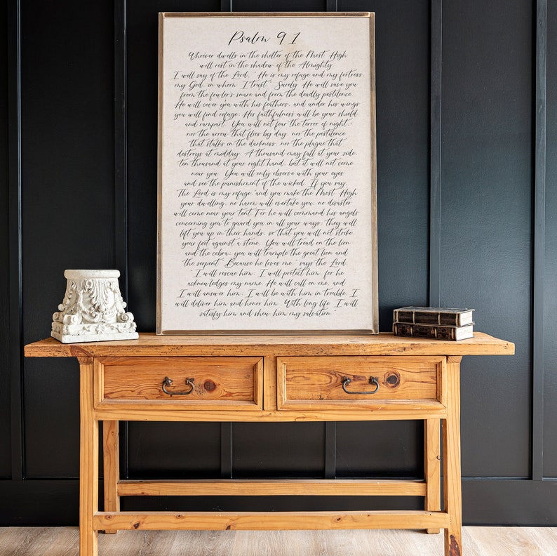 May include: A framed print of Psalm 91, a passage from the Bible, with a white background and black text. The text is written in a cursive font and includes the words "Who dwells in the shelter of the Most High" and "He will cover you with his feathers".