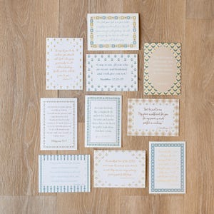 May include: A collection of rectangular cards with various Bible verses and decorative borders. The cards feature text in different fonts and colors, with floral and geometric patterns. The cards are arranged on a light wood surface.
