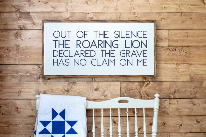 Może przedstawiać: Biały drewniany znak z napisem w kolorze granatowym, kt&oacute;ry brzmi "Out of the silence the roaring lion declared the grave has no claim on me". Znak wisi na drewnianej ścianie.