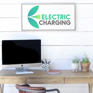 May include: A wooden desk with a computer, keyboard, and accessories. A sign above the desk reads "ELECTRIC CHARGING" in green and gray. Two small potted plants and a pen holder are on the desk.