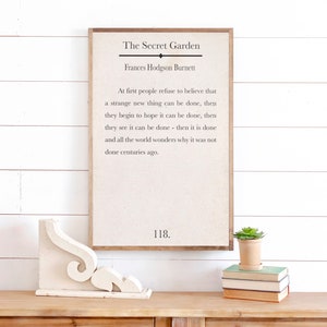 May include: A framed print with a white background and black text. The text reads "The Secret Garden" by Frances Hodgson Burnett. The quote reads "At first people refuse to believe that a strange new thing can be done, then they begin to hope it can be done, then they see it can be done - then it is done and all the world wonders why it was not done centuries ago." The number 118 is printed at the bottom of the print.