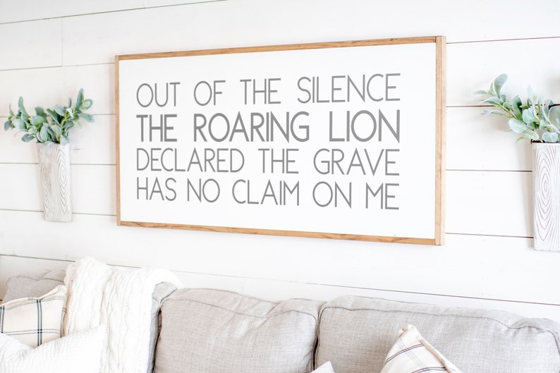 Może przedstawiać: Biały drewniany znak z drewnianą ramą wisi na białej ścianie. Znak zawiera tekst "OUT OF THE SILENCE THE ROARING LION DECLARED THE GRAVE HAS NO CLAIM ON ME" szarymi literami.