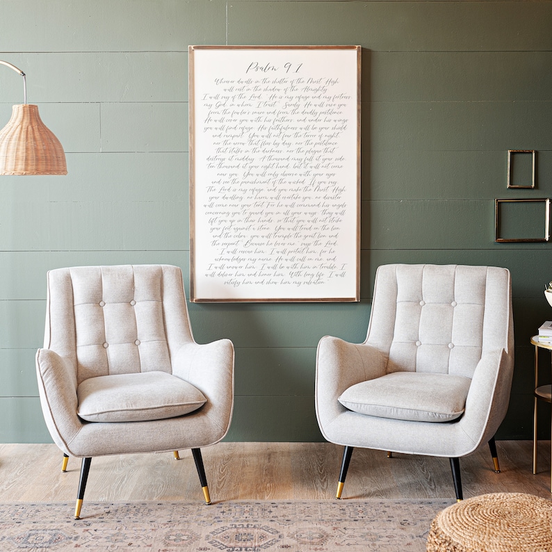 May include: A framed print of Psalm 91 in a white frame with a white background and black text. The print is hanging on a green wall between two light gray armchairs with gold legs.