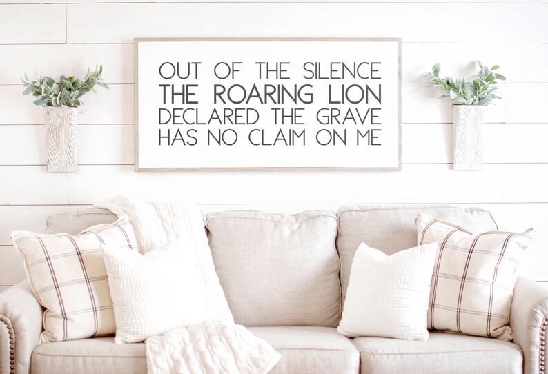Może przedstawiać: Wydruk w ramie z tekstem "OUT OF THE SILENCE THE ROARING LION DECLARED THE GRAVE HAS NO CLAIM ON ME" wiszący na białej ścianie z desek drewnianych nad beżową kanapą z białymi i brązowymi wzorzystymi poduszkami.