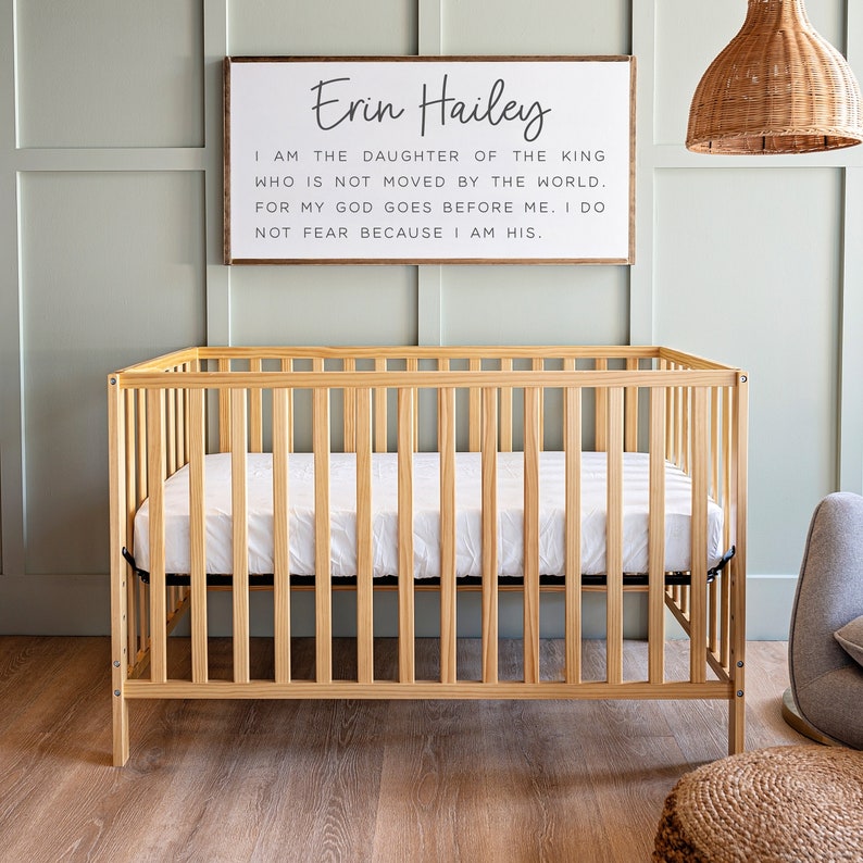 Może przedstawiać: Drewniane ł&oacute;żeczko z białym materacem i tabliczką nad nim, na kt&oacute;rej napisano: "Erin Hailey Jestem c&oacute;rką kr&oacute;la, kt&oacute;ry nie jest poruszany przez świat. Bo m&oacute;j B&oacute;g idzie przede mną. Nie boję się, bo jestem jego."