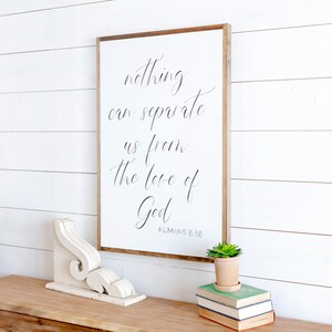 May include: White wooden sign with black calligraphy that reads "nothing can separate us from the love of God" with the scripture reference "ROMANS 8:36" below the text.