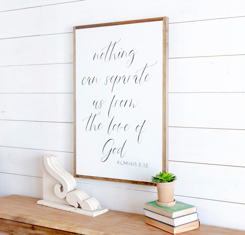 May include: White wooden sign with black calligraphy that reads "nothing can separate us from the love of God" with the scripture reference "ROMANS 8:36" below the text.