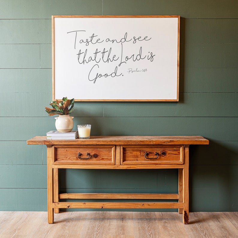 May include: A wooden console table with two drawers and a white framed sign above it that reads "Taste and see that the Lord is good. - Psalm 34:8"