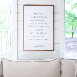 May include: A white wooden sign with a brown frame, featuring a bible verse from Isaiah 41:10. The verse reads "Fear not, for I am with you; be not dismayed, for I am your God; I will strengthen you, I will help you, I will uphold you with my righteous right hand."