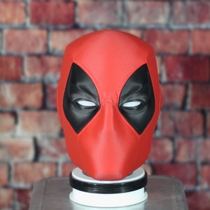 Könnte beinhalten: Eine rote und schwarze Deadpool-Maske mit strukturierter Oberfläche. Die Maske hat ein weißes Augen-Design.