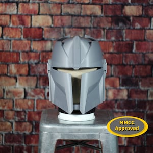 May include: A gray 3D printed helmet with a visor and a MMCC Approved sticker. The helmet is sitting on a silver stool.