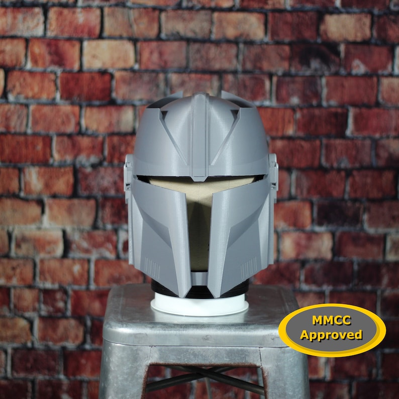 May include: A grey 3D printed helmet with a visor and an MMCC Approved sticker. The helmet is sitting on a silver stool.