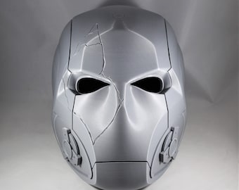 May include: A gray, futuristic-looking mask with a cracked design across the face. The mask has large eye openings and circular details on the sides. The overall design suggests a sci-fi or cosplay theme.