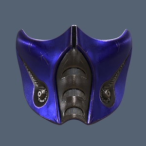 May include: A blue and black plastic mask with a metallic finish. The mask has a grid pattern on the front and a raised design on the sides.