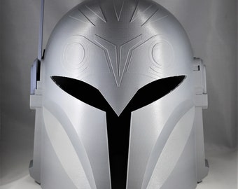 May include: A 3D printed helmet with a silver finish and a black visor. The helmet has a raised design on the top and a small antenna on the side.