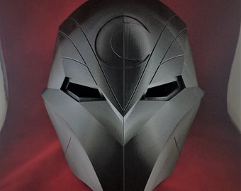 May include: A black 3D printed helmet with a crescent moon design on the front. The helmet has a sharp, angular design and is made of a smooth, matte material.