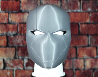 May include: A grey 3D printed helmet with a stylised design. The helmet has two eye holes and a pointed chin.