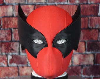 Peut inclure: Un masque de super-héros rouge et noir avec une surface texturée. Le masque a un masque pour les yeux noir avec une maille blanche recouvrant les yeux. Le masque a deux oreilles noires sur le dessus.