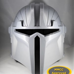 May include: A white plastic helmet with a black visor and a black stripe down the centre. The helmet has a textured surface and a raised design on the top. The helmet is labelled "MMCC Approved".
