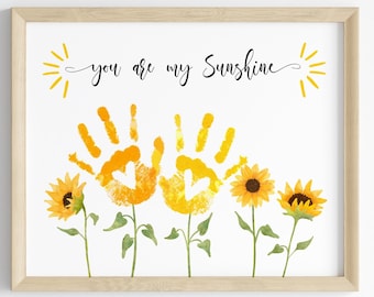 May include: A framed print with the text "You are my Sunshine" and two yellow handprints in the shape of sunflowers. The print features four sunflowers with green stems and leaves.