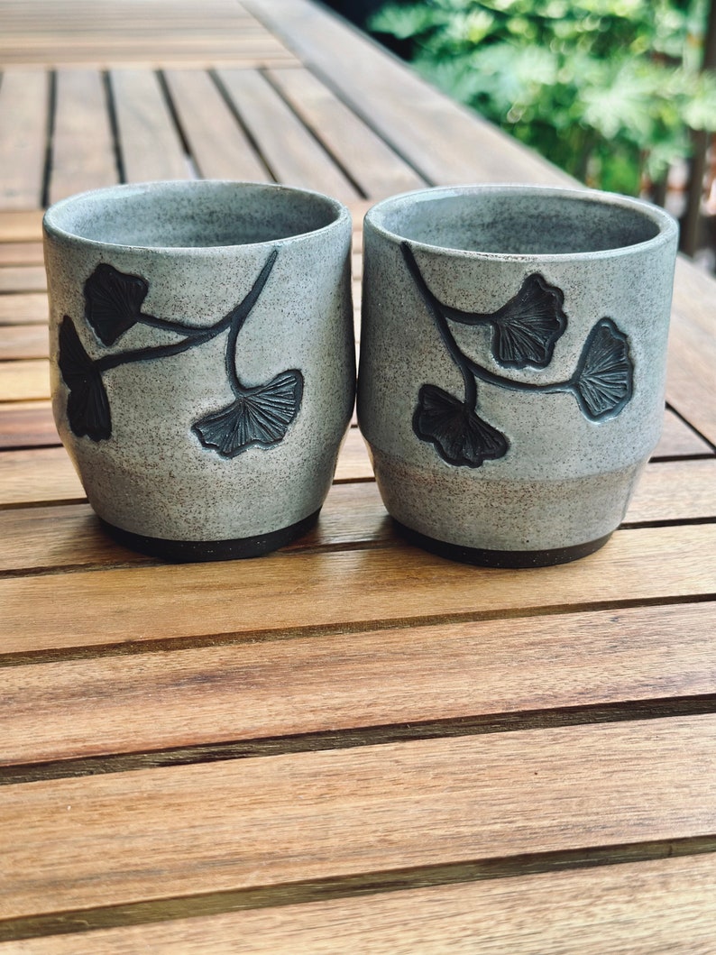 set of two handmade ceramic cups decorated with a speckled gray glaze and dark brown ginkgo carvings