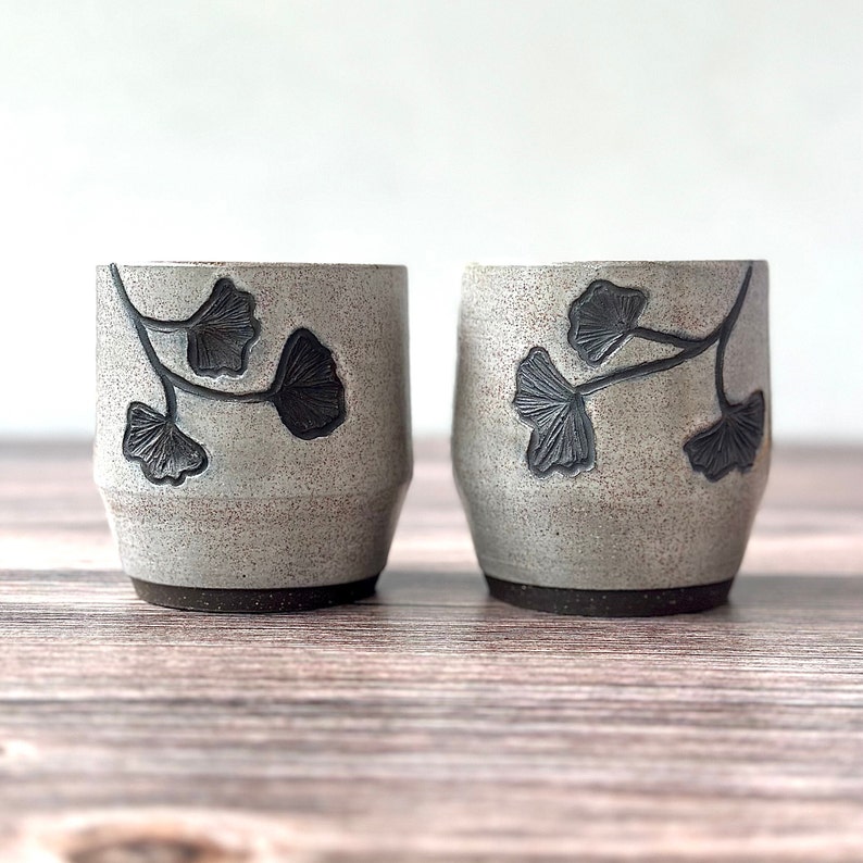 set of two handmade ceramic cups decorated with a speckled gray glaze and dark brown ginkgo carvings