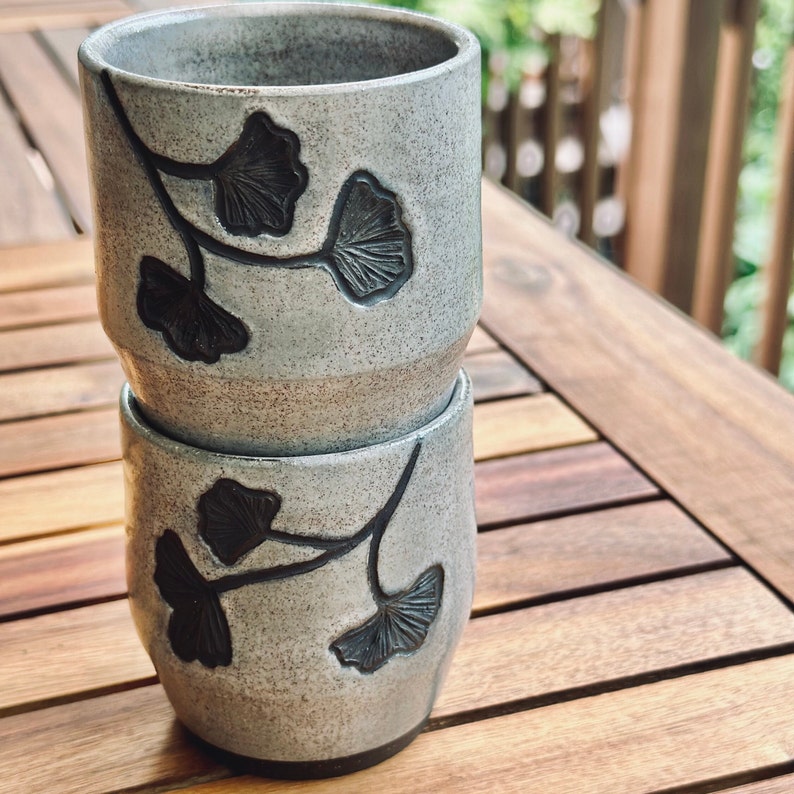 set of two handmade ceramic cups decorated with a speckled gray glaze and dark brown ginkgo carvings