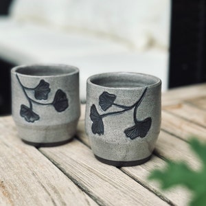 set of two handmade ceramic cups decorated with a speckled gray glaze and dark brown ginkgo carvings