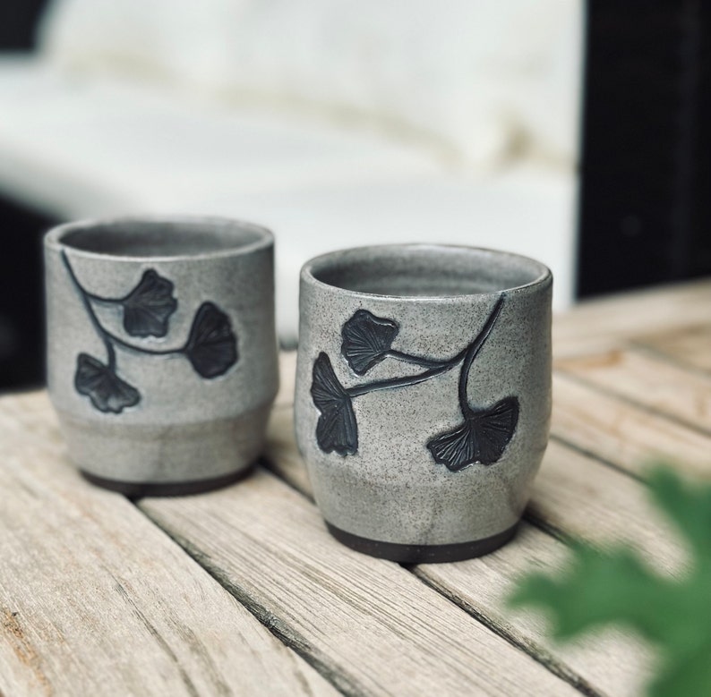 set of two handmade ceramic cups decorated with a speckled gray glaze and dark brown ginkgo carvings