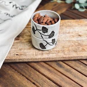May include: Two stacked ceramic bowls with a black floral design. The top bowl is filled with almonds.