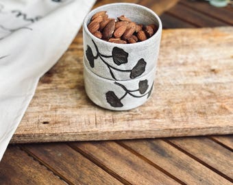 May include: Two stacked ceramic bowls with a black floral design. The top bowl is filled with almonds.